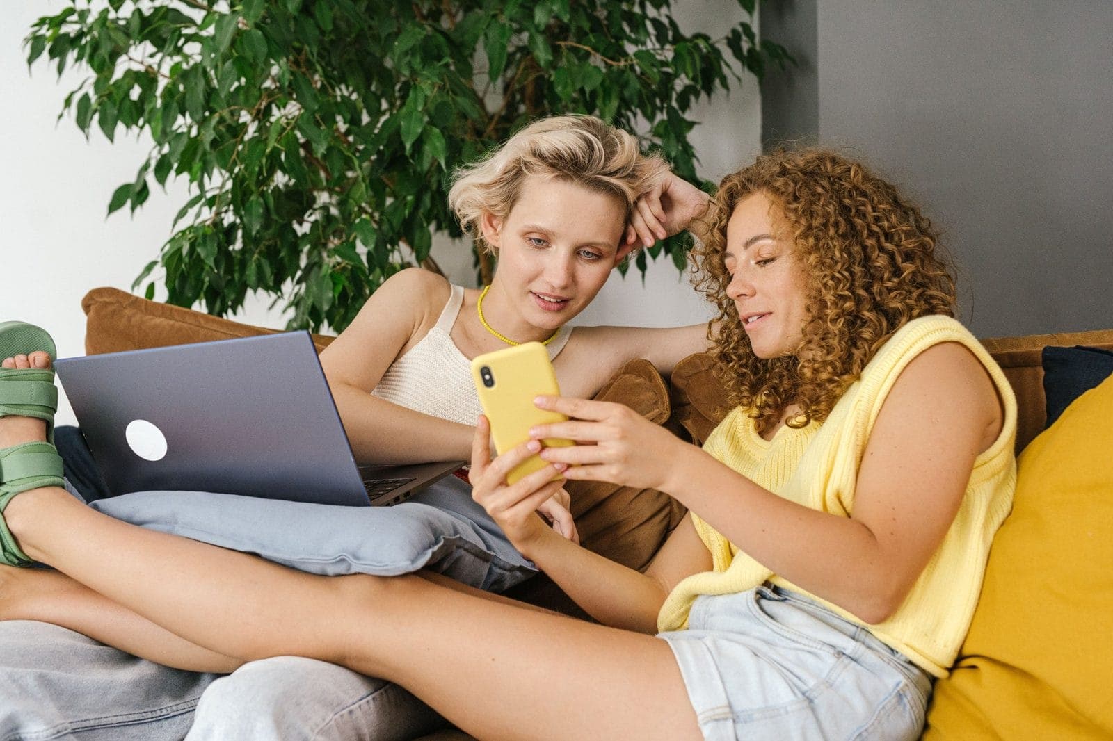 Two women relaxed at home, one with a laptop, one with a phone